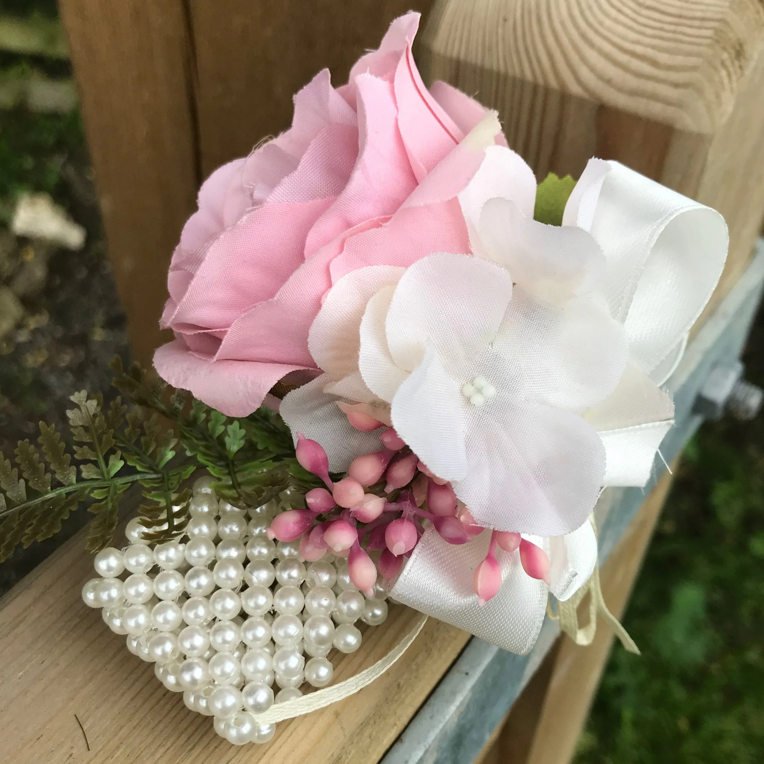 A wrist corsage featuring a dusky pink artificial silk rose